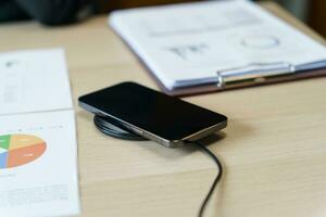 cargando móvil teléfono batería con inalámbrico cargando dispositivo en el mesa. teléfono inteligente cargando en un cargando almohadilla. móvil teléfono cerca inalámbrico cargador moderno estilo de vida tecnología concepto foto