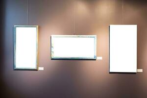 Blank picture frames on brown wall with glowing lamp, mock up photo