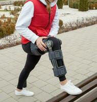 Woman wearing knee brace or orthosis after leg surgery, walking in the park photo