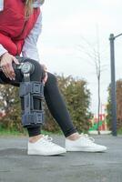 Woman wearing knee brace or orthosis after leg surgery, walking in the park photo