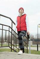 Woman wearing knee brace or orthosis after leg surgery, walking in the park photo