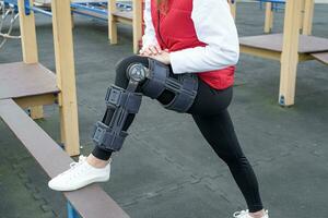 Woman wearing knee brace or orthosis after leg surgery, walking in the park photo