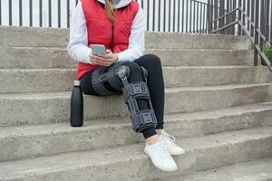 Woman wearing knee brace or orthosis after leg surgery, walking in the park photo