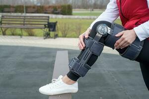 Woman wearing knee brace or orthosis after leg surgery, walking in the park photo