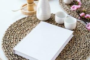 Book mockup design. Blank white book on dining table in asian style with tableware photo