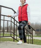 Woman wearing knee brace or orthosis after leg surgery, walking in the park photo