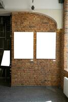 Blank picture frames on brick wall with glowing lamp, mock up photo