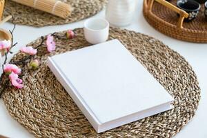 Book mockup design. Blank white book on dining table in asian style with tableware photo