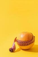 Fruit orange is wrapped with measuring tape on yellow background. photo