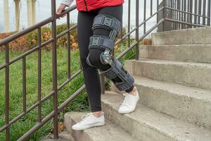 Woman wearing knee brace or orthosis after leg surgery, walking in the park photo