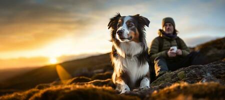 excursionismo con el perro, un joven hombre y su activo frontera collie perro sentado en acantilado rock a tomar un ver de amanecer después largo sendero trekking en el montaña picos ocupaciones con mascota. ai generativo foto