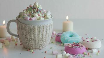 Sprinkles Falling onto Whipped Cream Chocolate Drink. Hot cocoa,  with candies and marshmallows. Colorful donuts on a white table surrounded with candles at home video