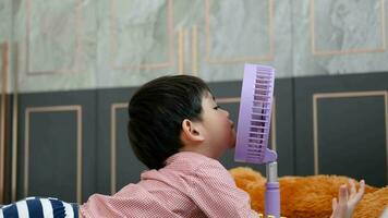 asiatisch Junge Lügen auf das Matratze auf ein heiß Tag spielen mit ein tragbar Ventilator glücklich video