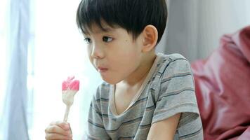 un asiatique garçon est en mangeant délicieux la glace crème dans une chaise. video