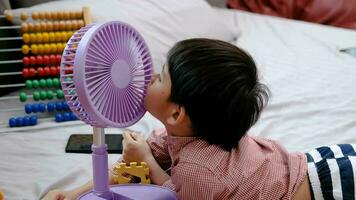 asiatisk pojke liggande på de madrass på en varm dag spelar med en bärbar fläkt lyckligt video
