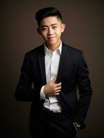 sonriente joven hombre de asiático descendencia vestido en traje en gris antecedentes ai generativo foto
