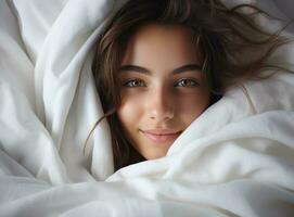 young woman sleeping under a white blanket in a bed photo