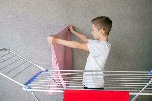 Cute boy doing household chores, hanging wet clothes on the dryer photo