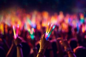 A close-up shot of hands holding glow sticks in the air at a rave party with a blurry crowd of people dancing in the background. Generative Ai photo