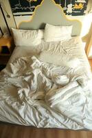 messy hotel bed. White pillow. White roll. white blanket. photo