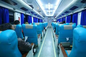 Executive class train interior with blue seats, armrests, luggage racks, monitor screens, air conditioning, and lights that extend on the ceiling photo