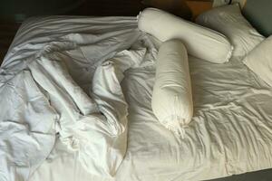 messy hotel bed. White pillow. White roll. white blanket. photo