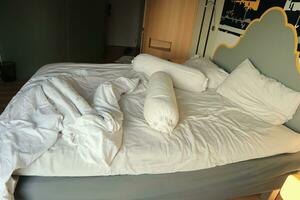 messy hotel bed. White pillow. White roll. white blanket. photo