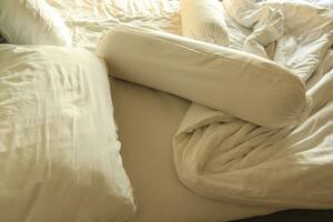 messy hotel bed. White pillow. White roll. white blanket. photo