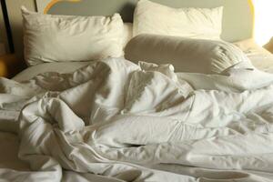 messy hotel bed. White pillow. White roll. white blanket. photo