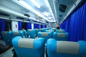 Executive class train interior with blue seats, armrests, luggage racks, monitor screens, air conditioning, and lights that extend on the ceiling photo