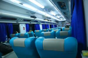 Executive class train interior with blue seats, armrests, luggage racks, monitor screens, air conditioning, and lights that extend on the ceiling photo