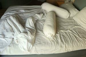messy hotel bed. White pillow. White roll. white blanket. photo