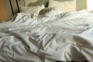 messy hotel bed. White pillow. White roll. white blanket. photo