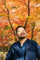 asiático hombre debajo arce árbol hojas durante otoño con color cambio en hoja en naranja amarillo y rojo, que cae natural antecedentes foto