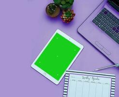 Top view of a streamlined work-from-home workspace with essential gadgets and a green screen setup. This minimalist arrangement is perfect for efficient remote work, virtual meetings, creatives. photo