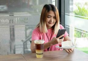 mujer participación pastel y teléfono inteligente tomar foto, usando tecnología teléfono móvil subir imágenes en social medios de comunicación a café, relajación vacaciones contento estilo de vida concepto. foto