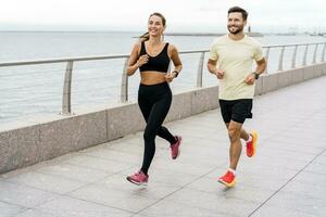 Runners are a man and a woman in sportswear and running shoes, in full height. Athletes are strong people who work out jogging together.Using a fitness watch. photo