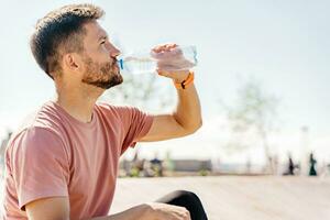 entrenador bebidas agua desde un botella, descanso descanso. atleta corredor formación en ropa de deporte. un deportivo hombre corriendo un lote. hombre corriendo en el ciudad Fresco aire. foto