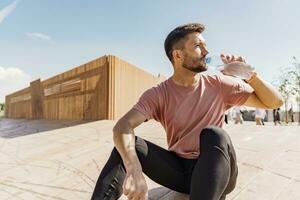 Break rest coach drinks water from a bottle. Athlete runner training in sportswear. A sporty man running a lot. Man running in the city fresh air. photo