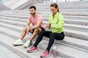 utilizando inteligente relojes y un aptitud aplicación masculino y hembra Atletas tren en aptitud y correr. equipo ejercicios de un joven Pareja. personas en ropa de deporte juntos, físico educación y Deportes. foto