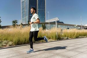 A sporty man running a lot in running shoes. Man running in the city fresh air. Athlete runner full-length workout in sportswear. Uses a fitness watch and an app. photo