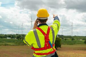 A smart engineer with protective helmet on head, using smartphone at electrical turbines field photo