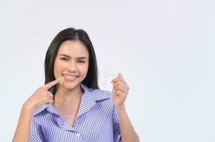 Young smiling woman holding invisalign braces over white background studio, dental healthcare and Orthodontic concept. photo