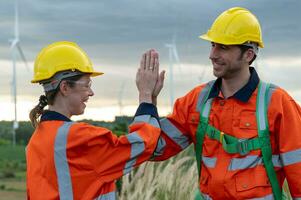 Smart engineers with protective helmet cheerfully giving high five at electrical turbines field photo
