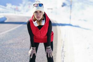 Athletic female in outerwear on road in winter mountains photo