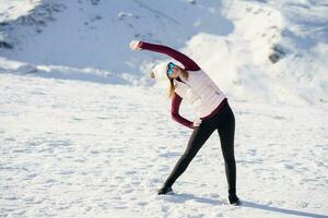 Young woman standing and doing exercise on snow in highlands photo