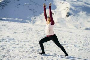 Slim woman stretching in warrior pose over snowy mountains photo