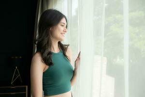 Portrait of a beautiful asian woman in green shirt standing near the window photo