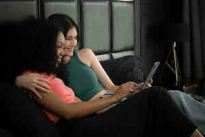 Two young women sitting on the bed in bedroom and using a digital tablet. photo