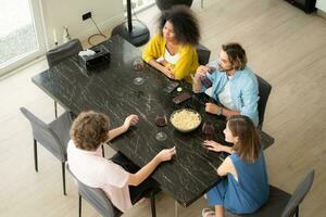 parte superior ver de multiétnico grupo de amigos sentado a mesa y teniendo cena juntos a hogar foto